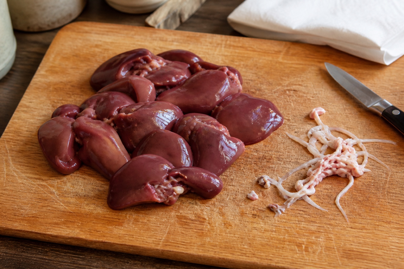 Зачищенная куриная печень на доске, рядом срезанные белые протоки и плёнки